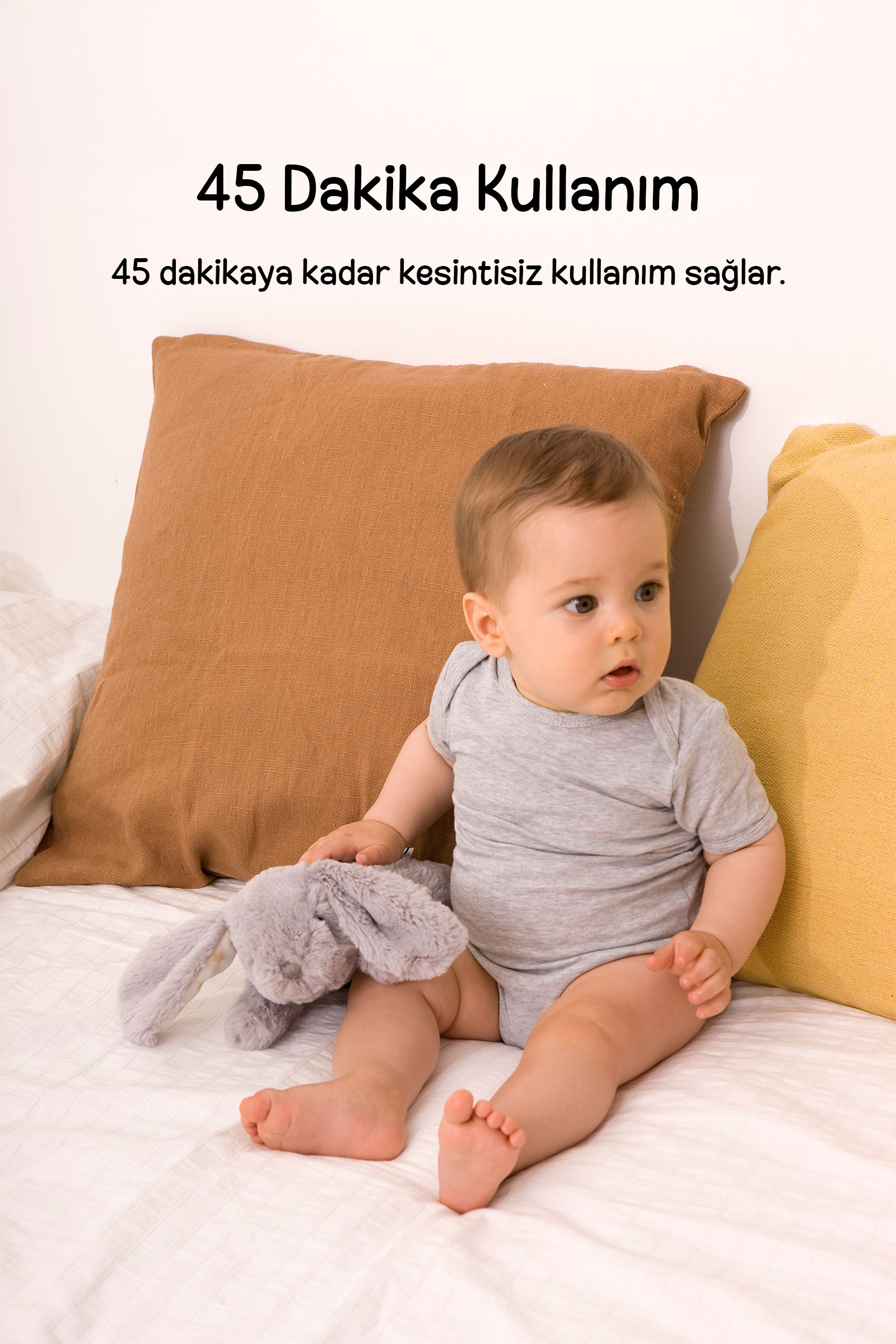 Gri zıbınlı bebek, yastıklı yatakta oturup peluş oyuncak tutuyor, üzerinde Türkçe metin var.