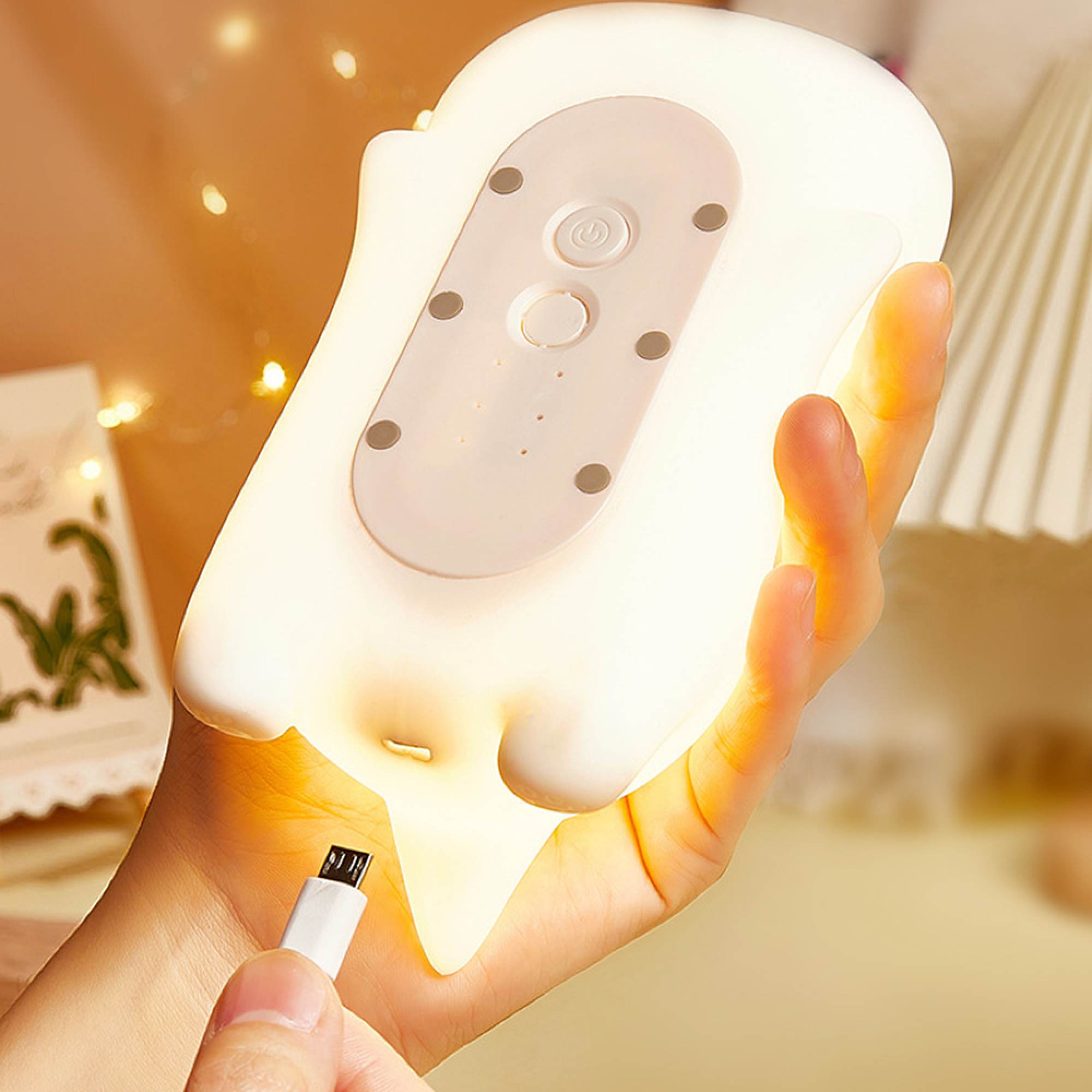 Eine Hand hält eine weiße, leuchtende Lampe mit USB-Kabel und Steuerungsfeld.