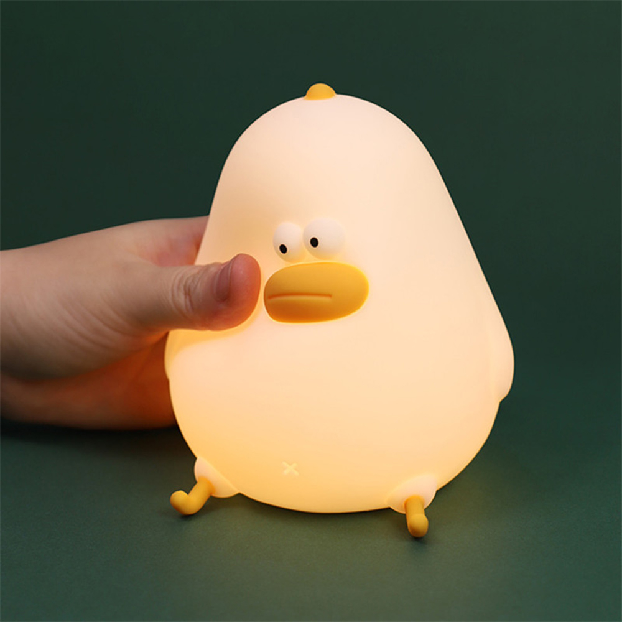 Eine Hand berührt eine weiche, gelbe Enten-Nachtlampe auf dunklem Hintergrund.
