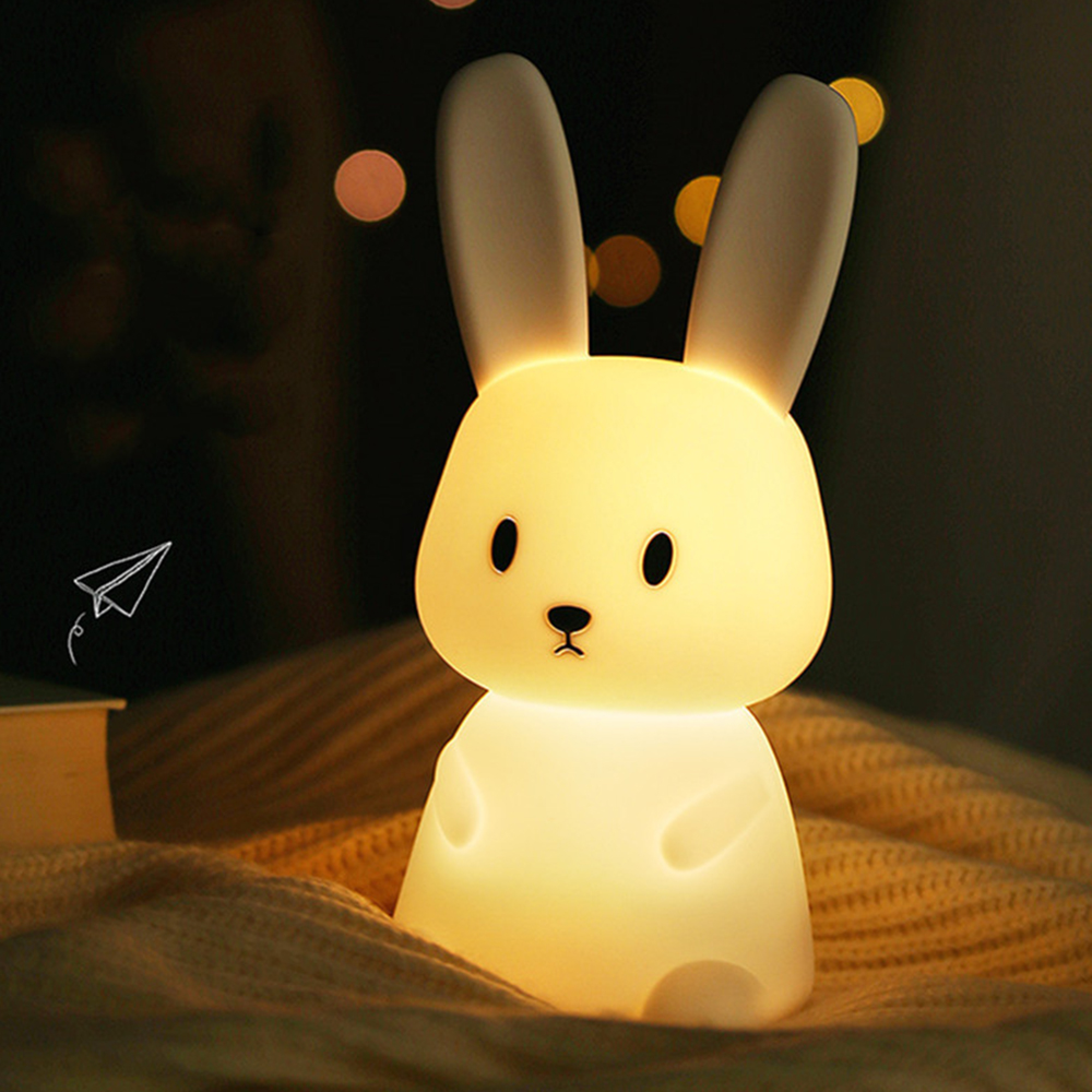 Eine niedliche, hell leuchtende Hasen-Nachtlampe auf einer Decke mit verschwommenem Hintergrund.