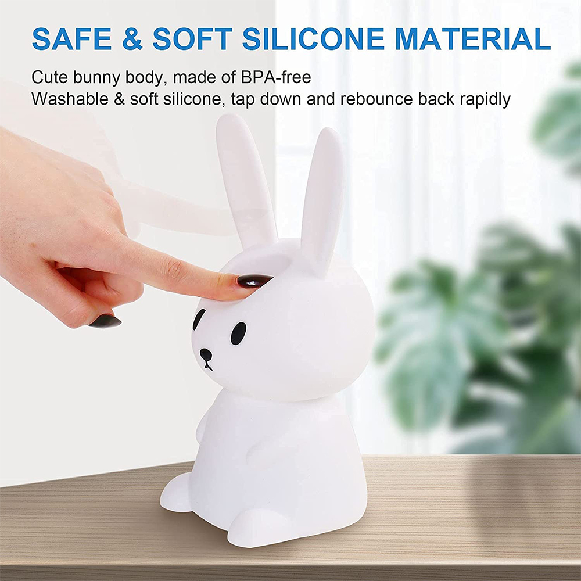 Ein finger drückt auf eine weiche, weiße Silikonhasen-Lampe auf einem Holztisch vor einem unscharfen Hintergrund.