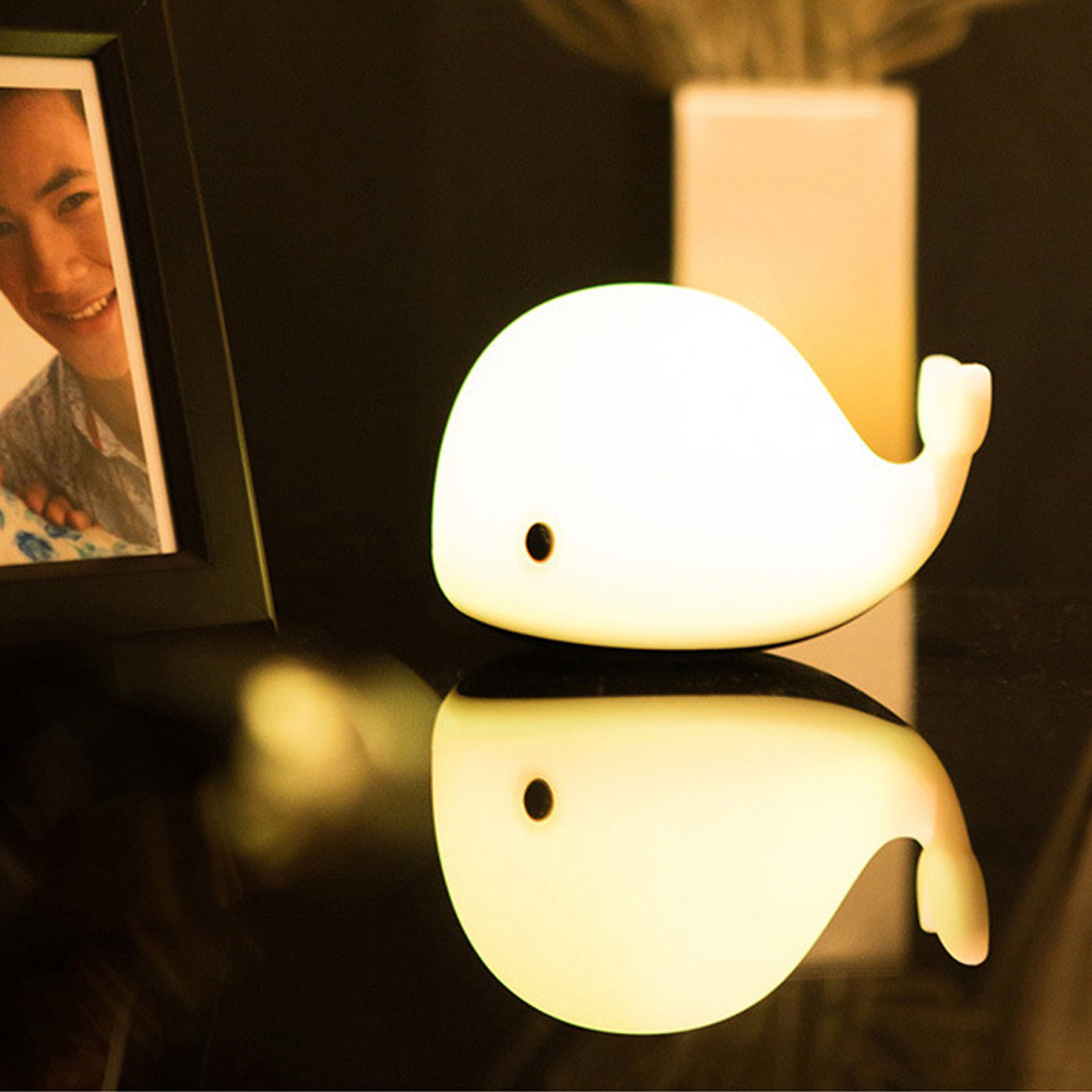 Eine Leuchtende Wal-Lampe steht auf einem dunklen Tisch mit Spiegelung.