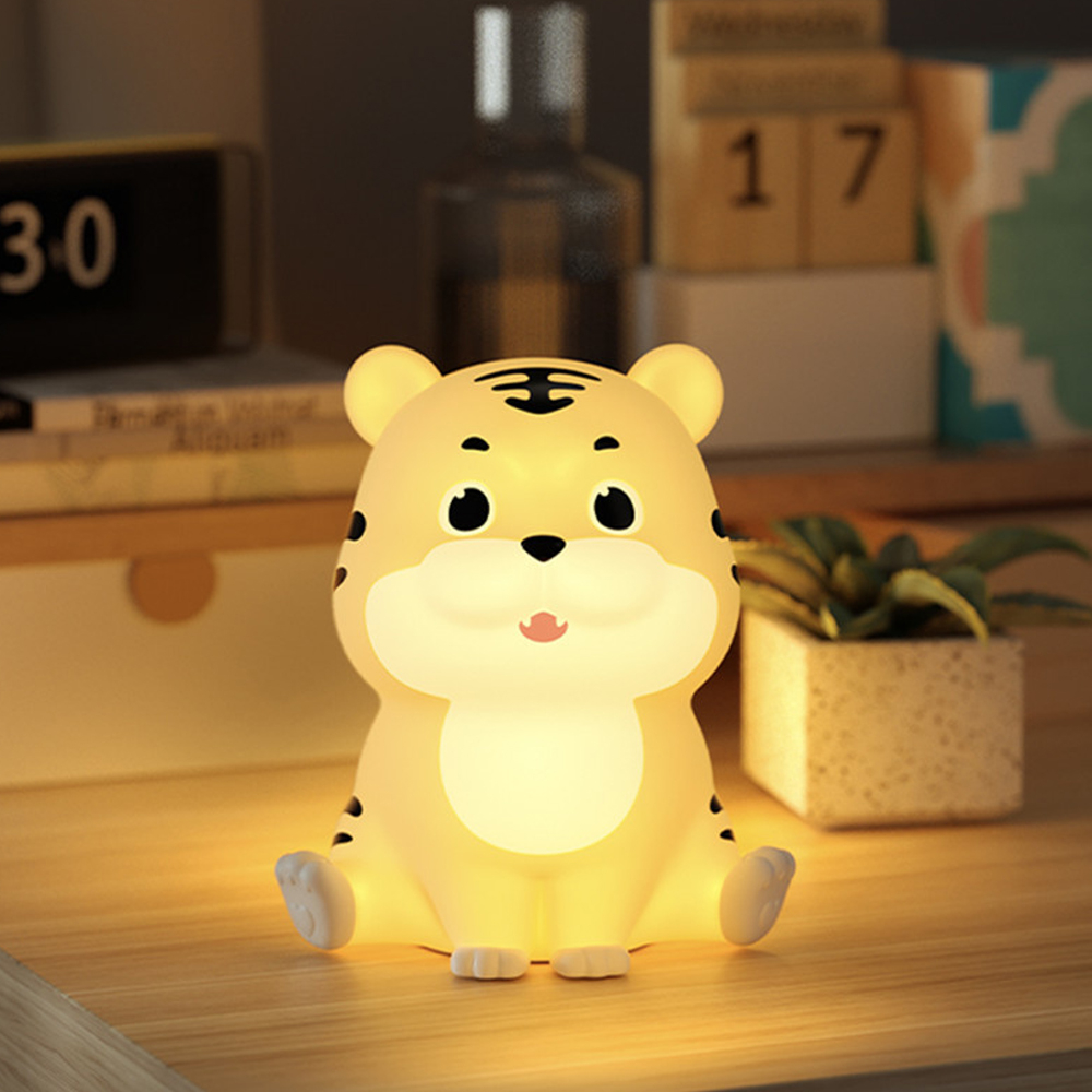 Eine niedliche, leuchtende Tiger-Nachtlampe sitzt auf einem Holztisch, im Hintergrund stehen ein Kalender und Pflanzen.