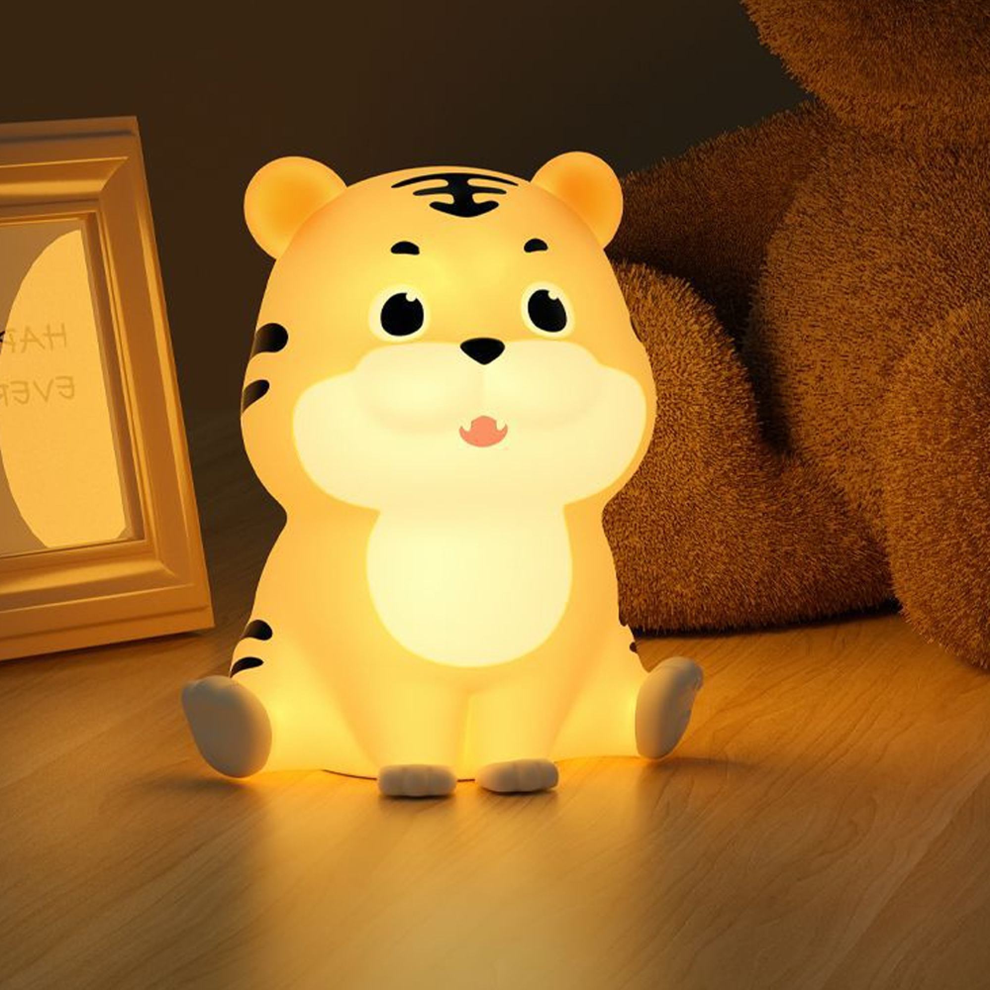 Eine niedliche, leuchtende Tiger-Nachtlampe sitzt auf dem Boden neben einem Bilderrahmen und einem Plüschtier.