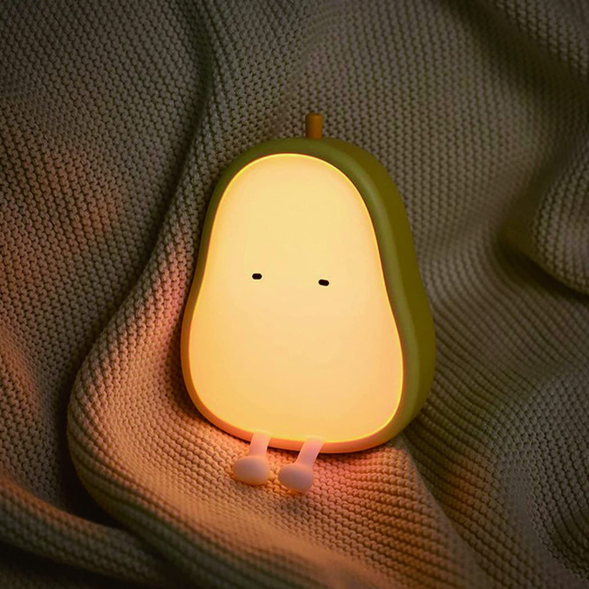 Ein leuchtendes birnenförmiges Nachtlicht mit kleinen Füßen liegt auf einer kuscheligen Decke.