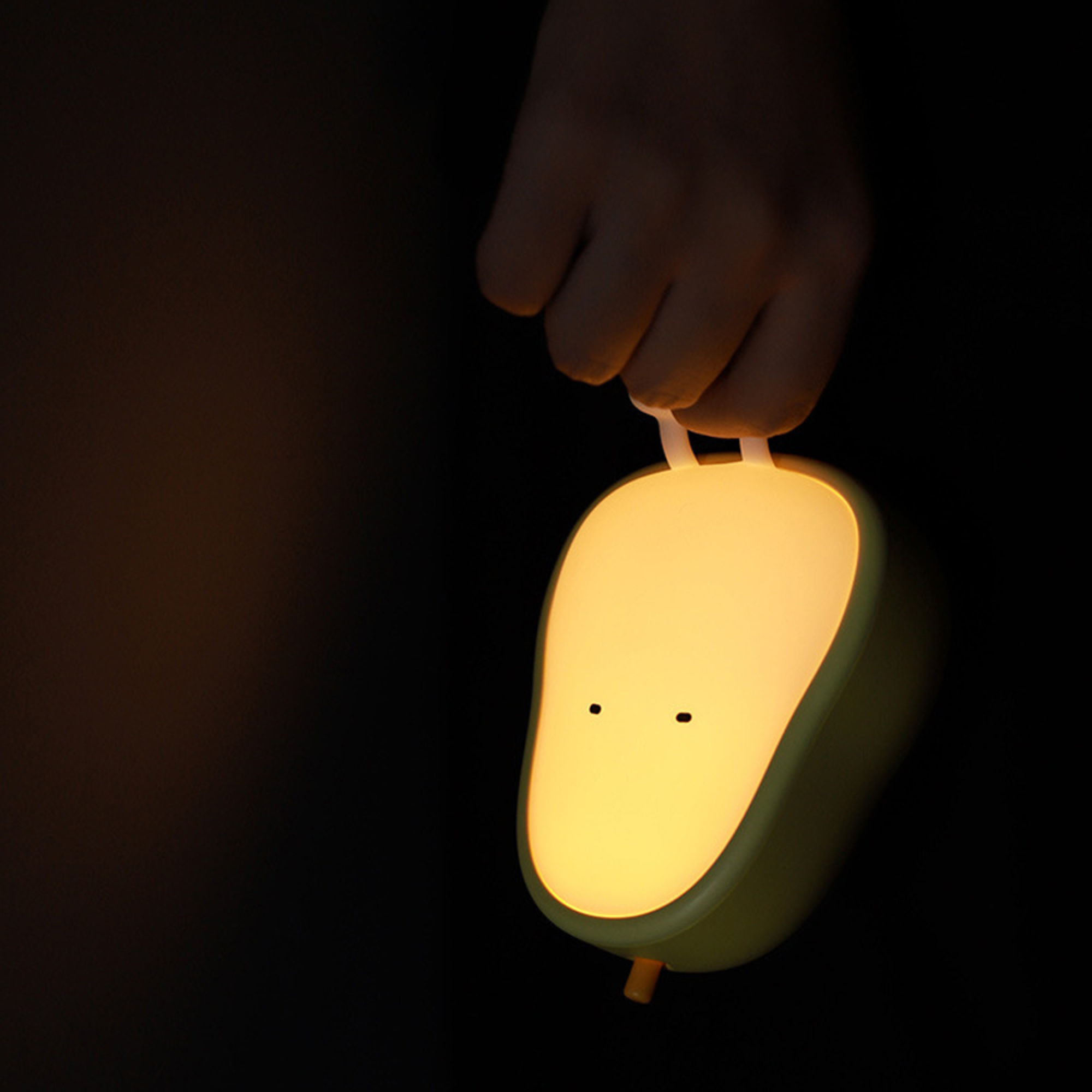 Eine Hand hält eine niedliche, gelbe Birnen-Nachtlampe mit kleinen Augen und warmem Licht im Dunkeln.