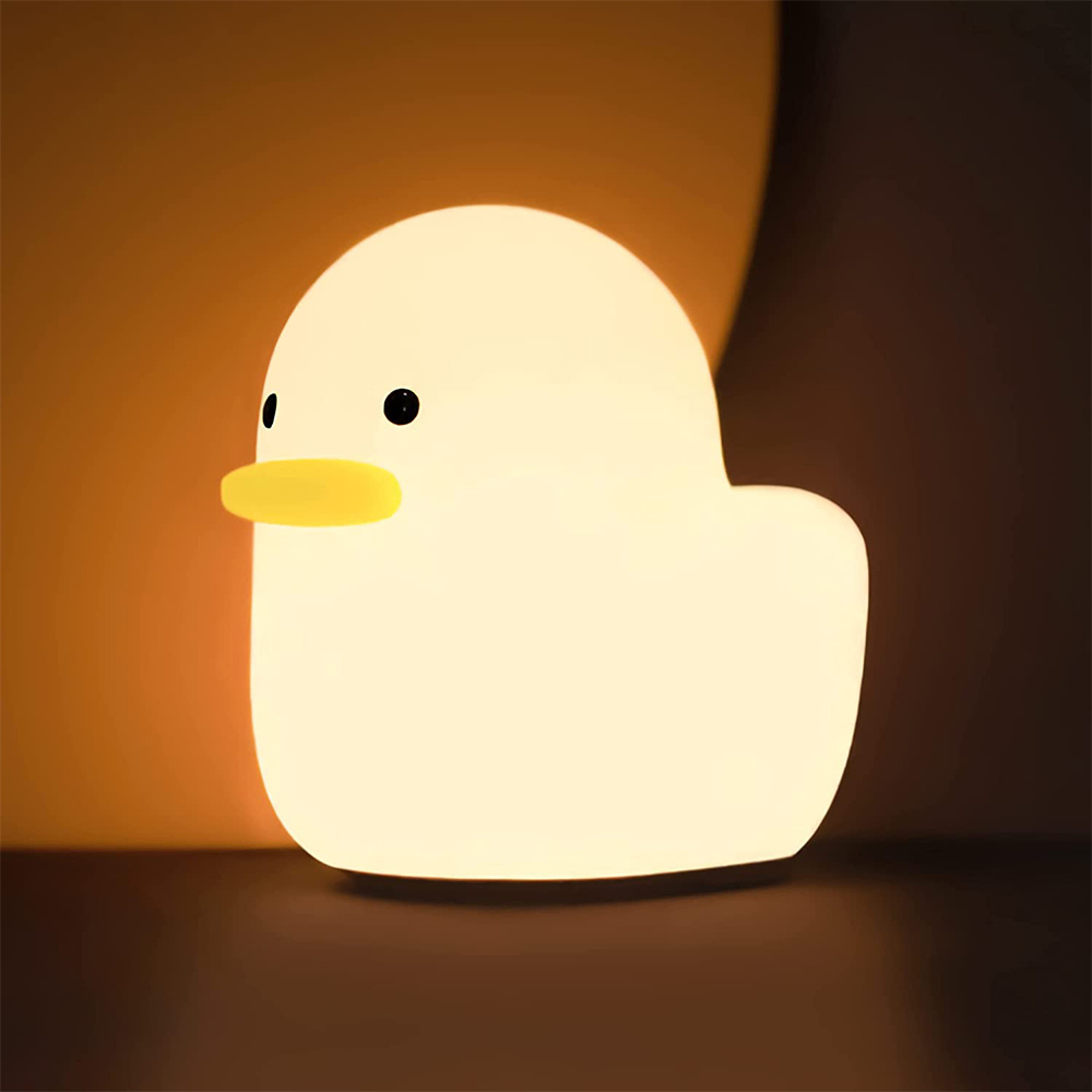 Eine kleine, warm leuchtende Enten-Nachtlampe steht vor einer dunklen Wand.
