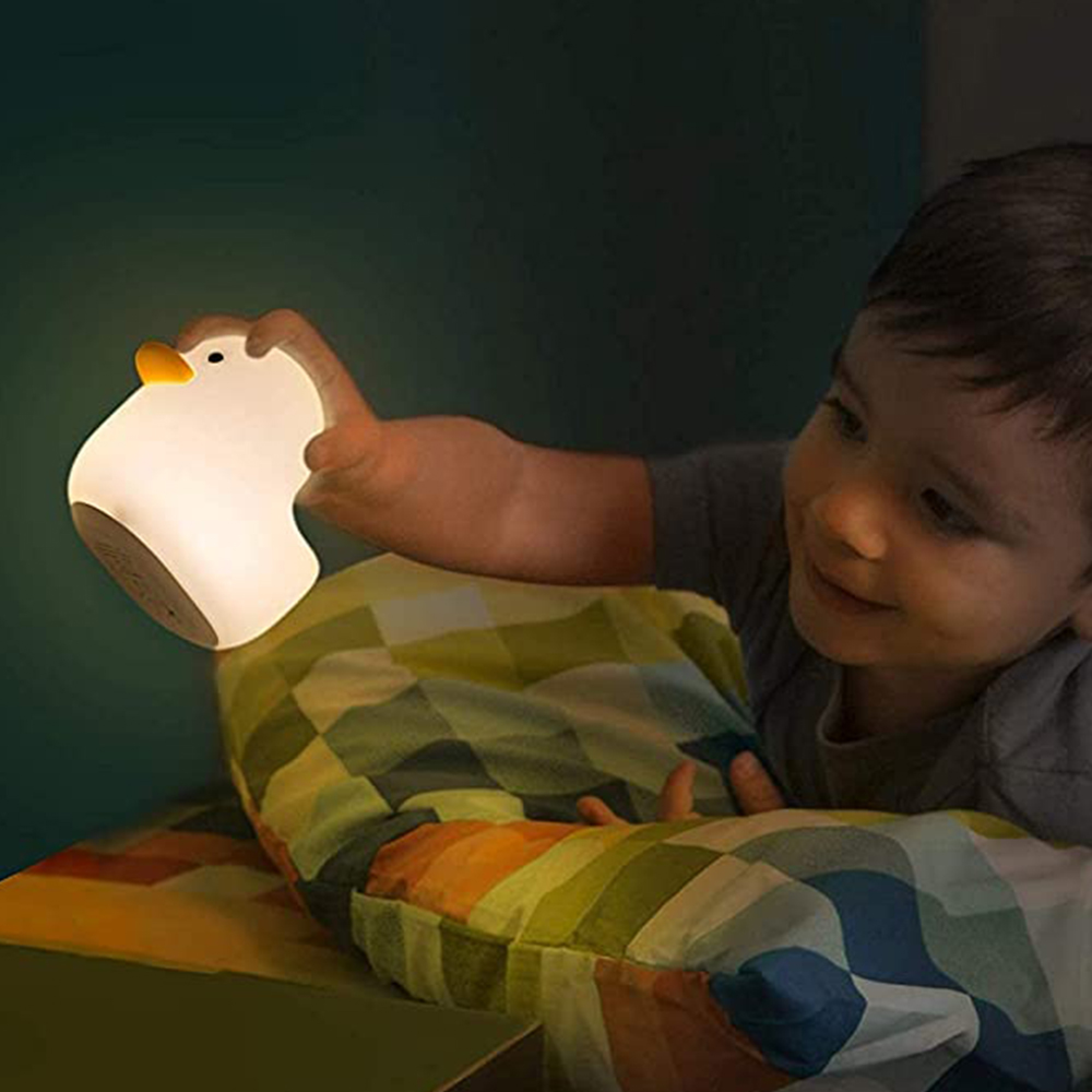 Ein Junge liegt im Bett und hält eine leuchtende, enteiförmige Nachtlampe in der Hand.