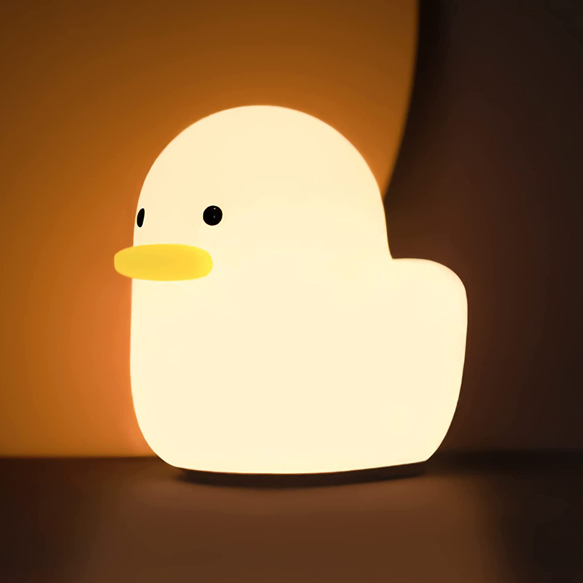 Eine weiße Enten-Nachtlampe mit gelbem Schnabel leuchtet warm vor einem dunklen Hintergrund.