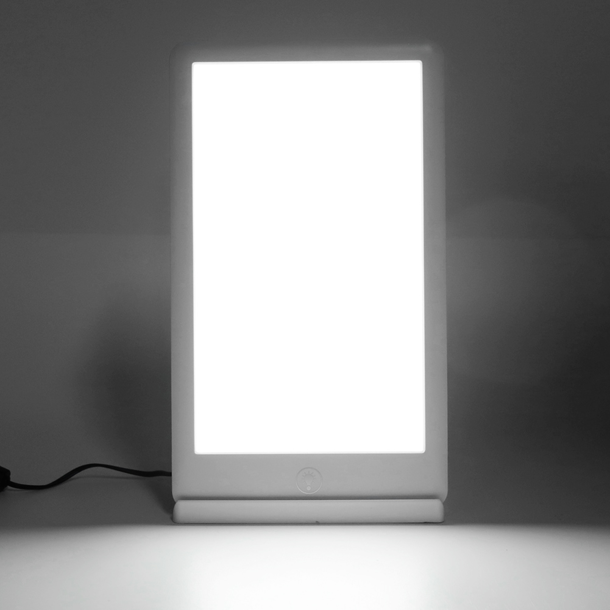 Eine weiße, leuchtende Tageslichtlampe steht auf einem Tisch vor dunklem Hintergrund.