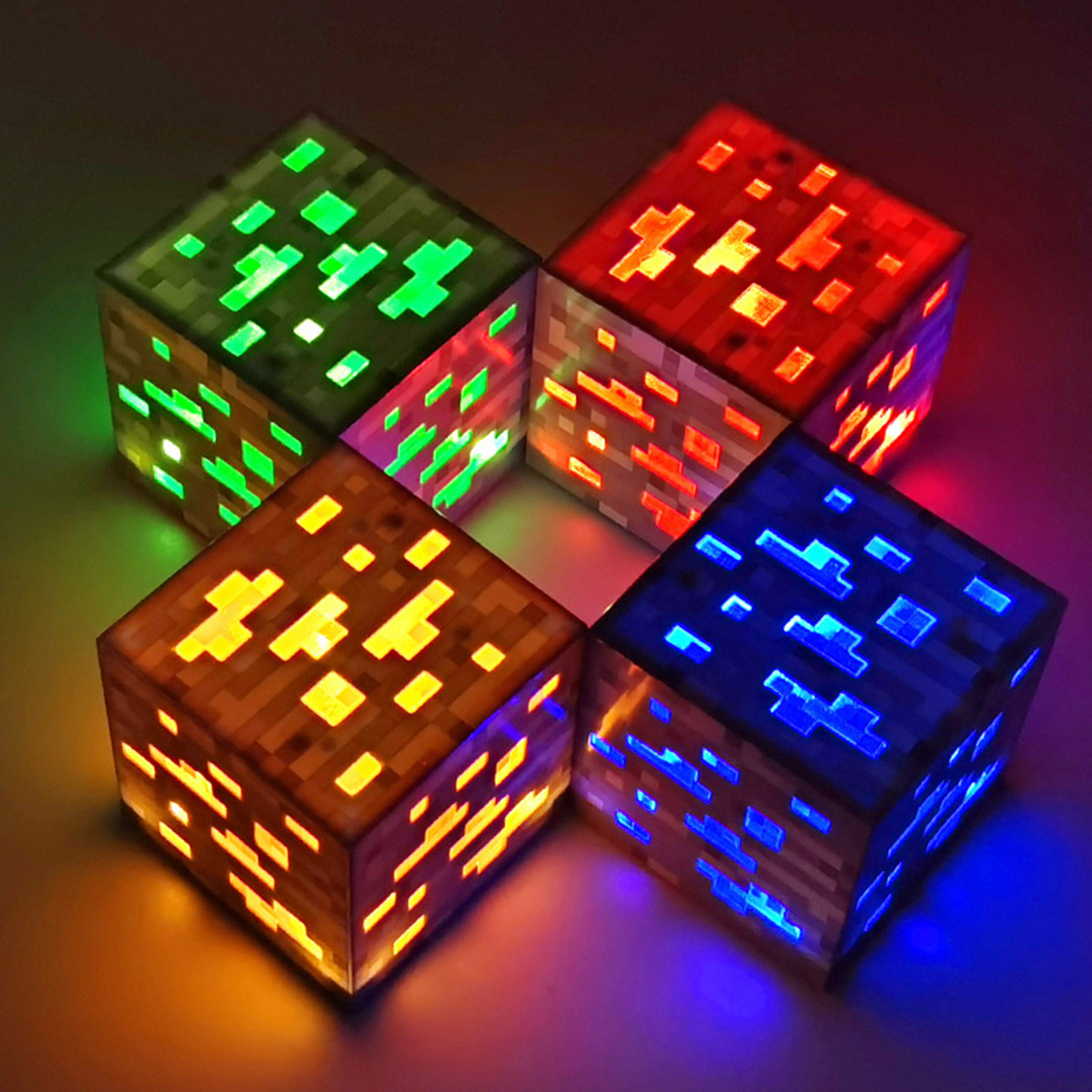 Vier leuchtende Minecraft-Erzwürfel in Grün, Rot, Gelb und Blau auf dunklem Hintergrund.