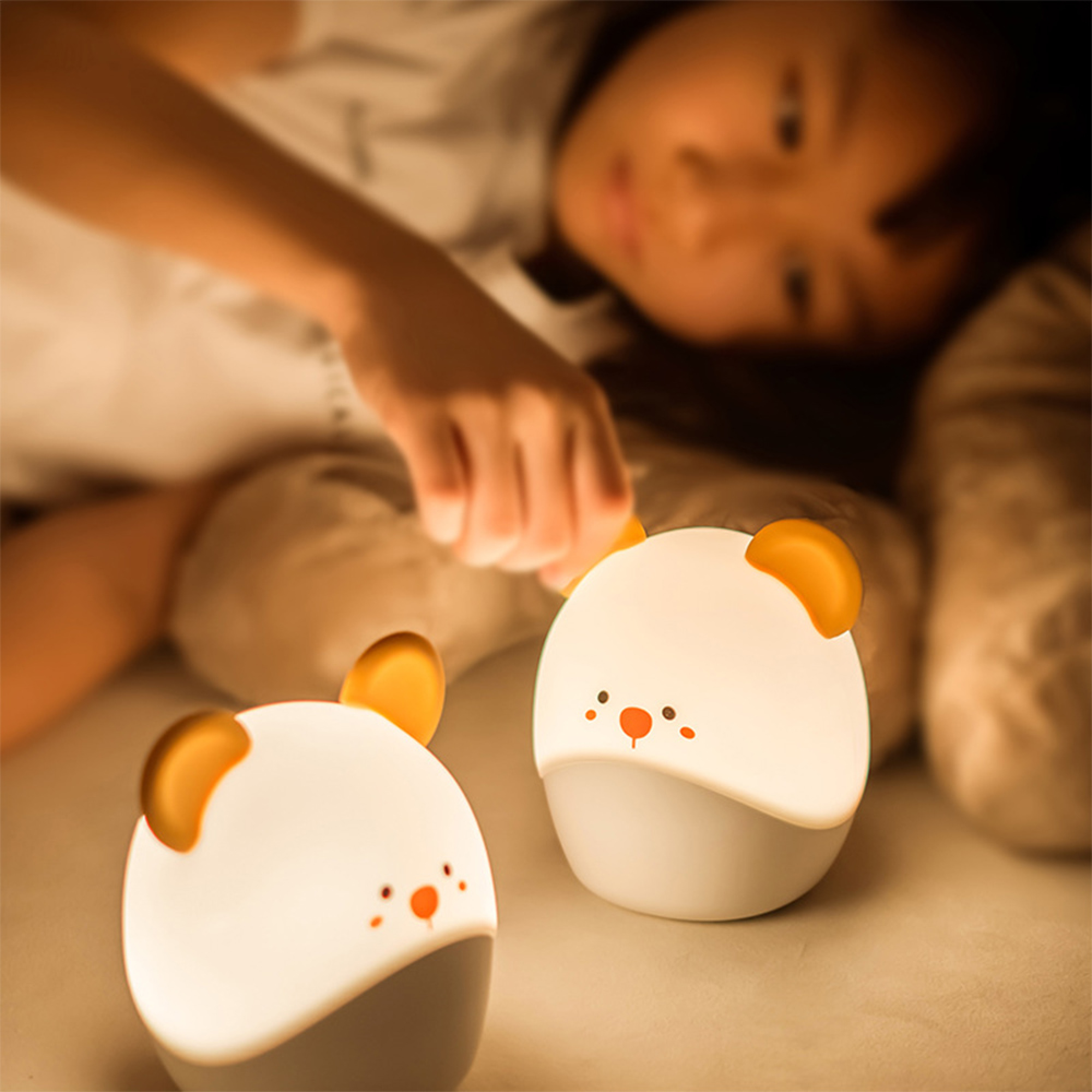 Ein junges Mädchen im Bett berührt eine von zwei leuchtenden, süßen tierförmigen Nachtlampen.