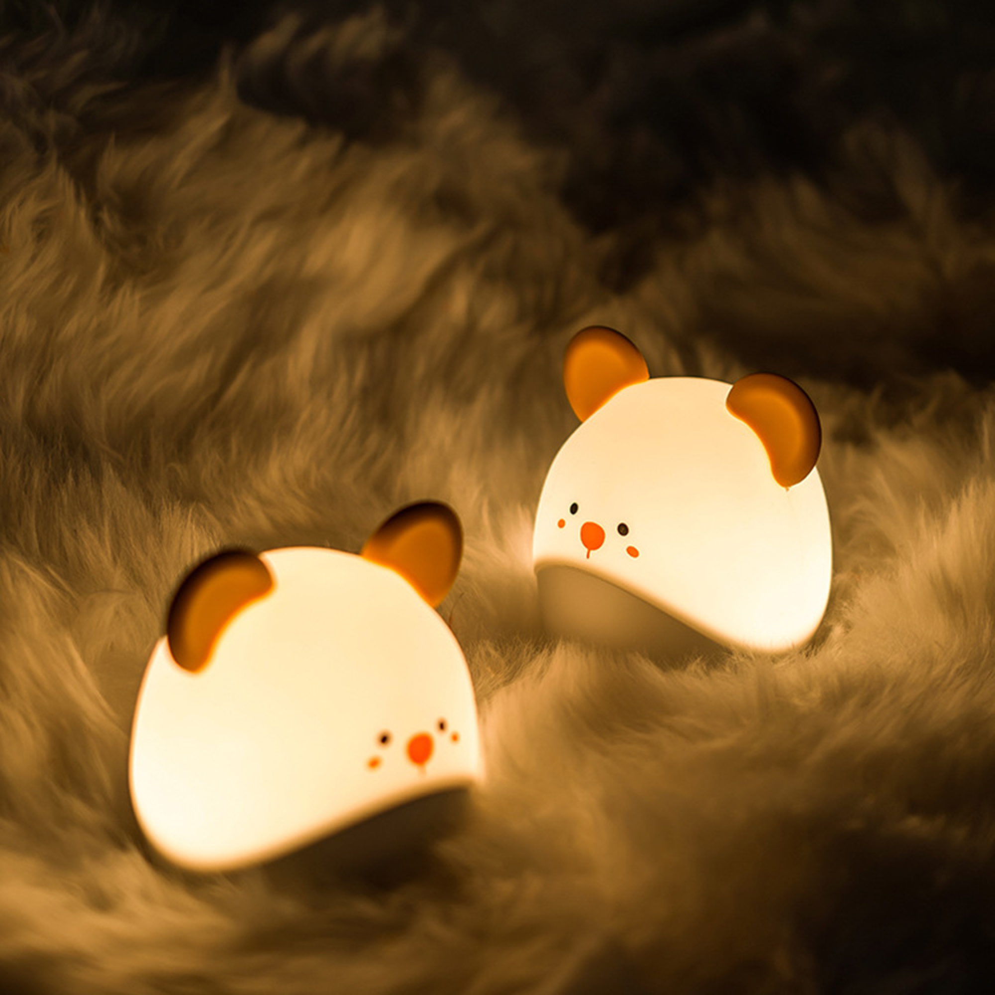 Zwei glowende Bären-Nachtlichter sitzen auf einer weichen, flauschigen Decke.