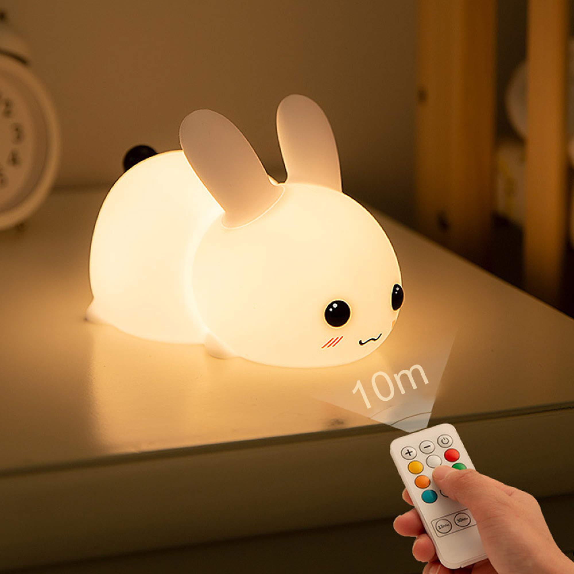 Ein leuchtendes Hasennachtlicht auf einer Oberfläche, gesteuert von einer kleinen Fernbedienung in einer Hand.
