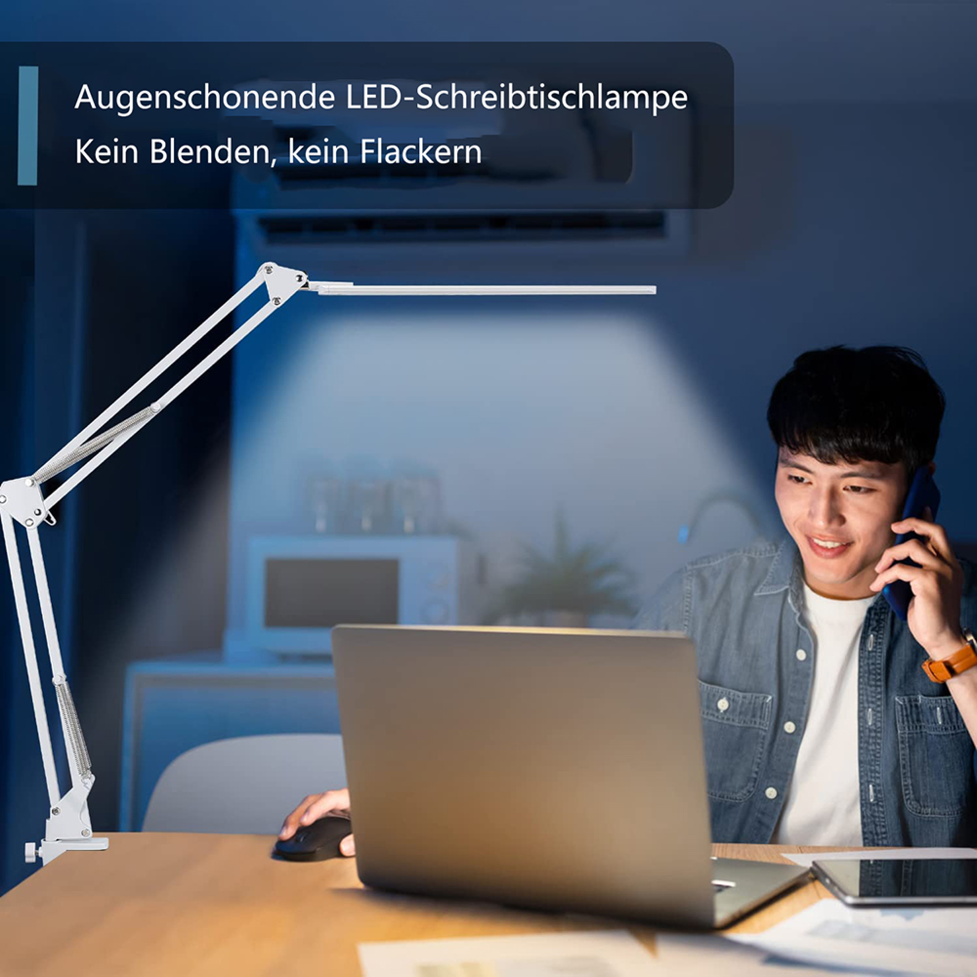 Ein Mann sitzt an einem Laptop und telefoniert, während eine weiße LED-Schreibtischlampe den Tisch beleuchtet.