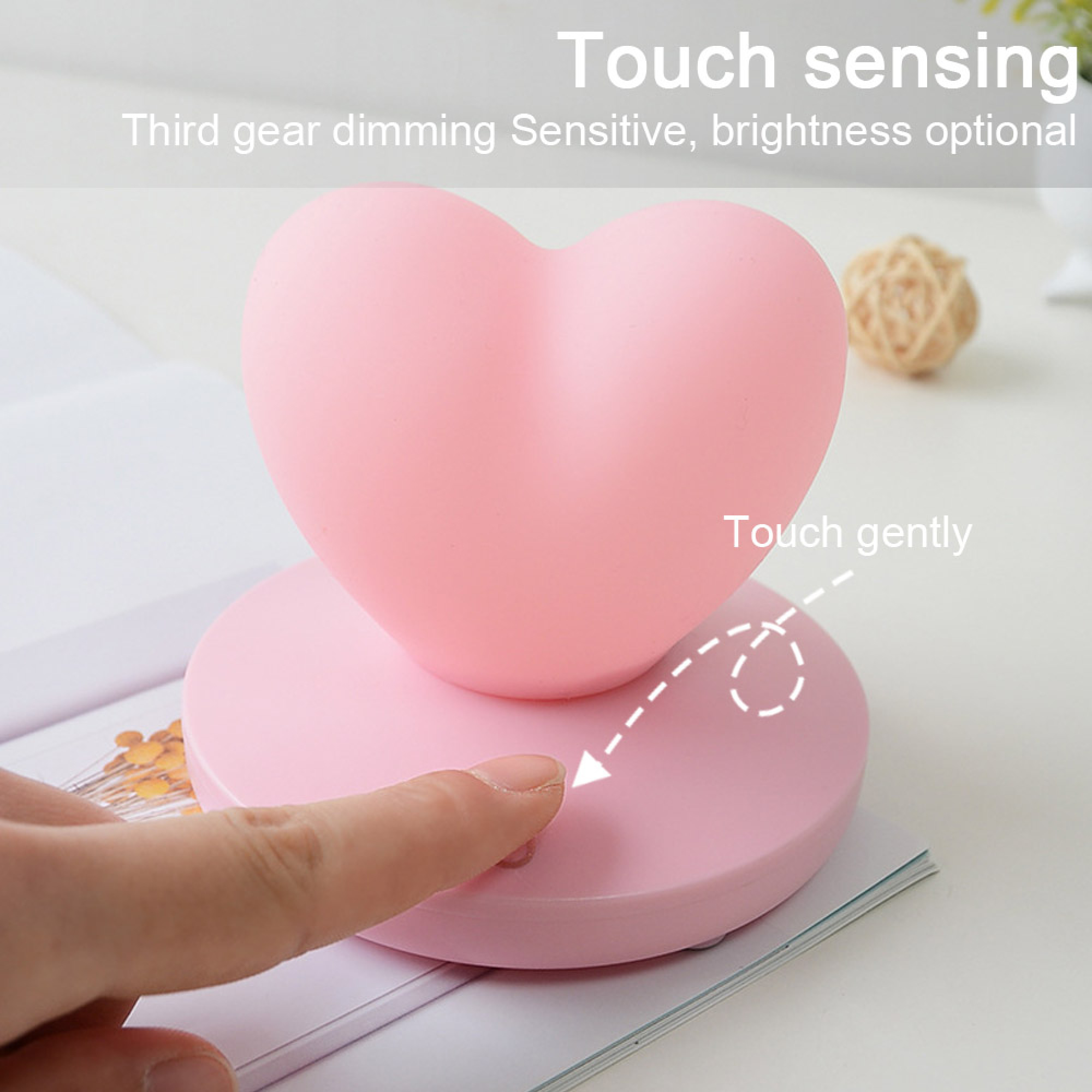 Ein Finger berührt die Basis einer rosa herzförmigen Lampe auf einem Buch.