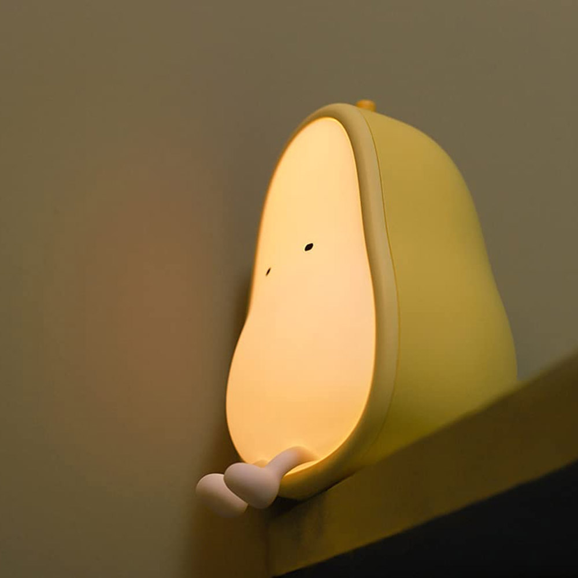 Eine gelbe, birnenförmige Nachtlampe sitzt mit kleinen Beinen auf einem Regal.