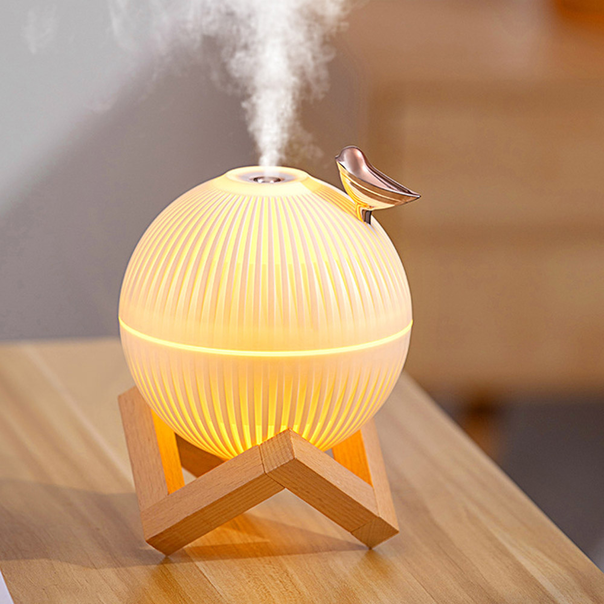 Ein runder, leuchtender Luftbefeuchter mit goldenem Vogel auf Holzständer stößt auf Holztisch Nebel aus.