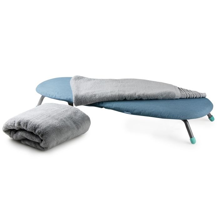 Ein blauer Campingtisch mit grauen Decken darauf und einer weiteren Decke daneben vor weißem Hintergrund.