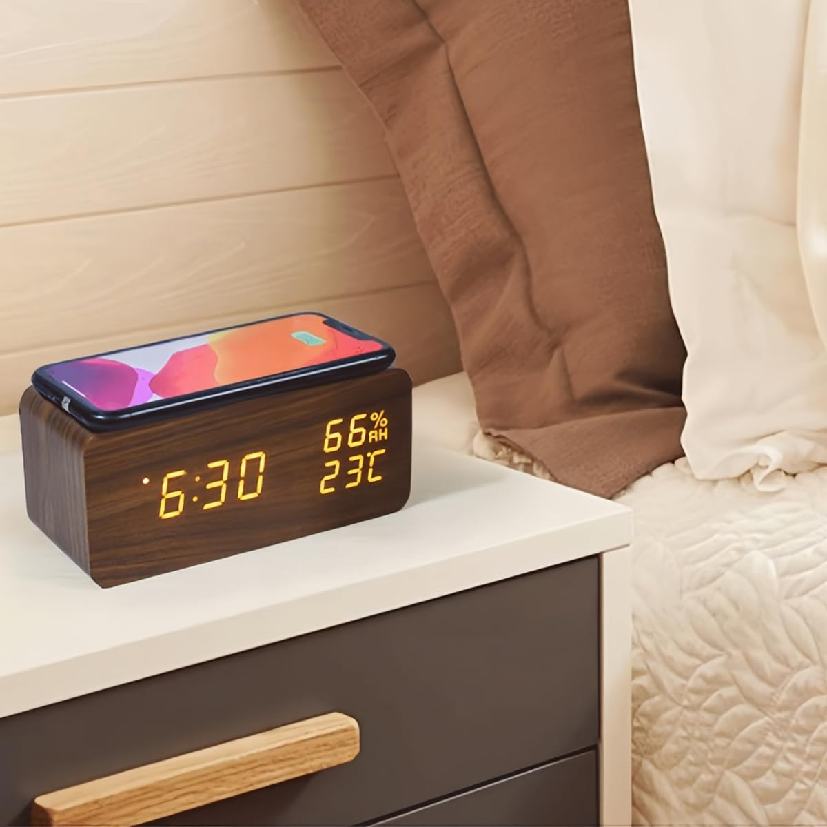 Ein Holz-Wecker mit digitaler Anzeige auf einem Nachttisch, mit einem Smartphone darauf.