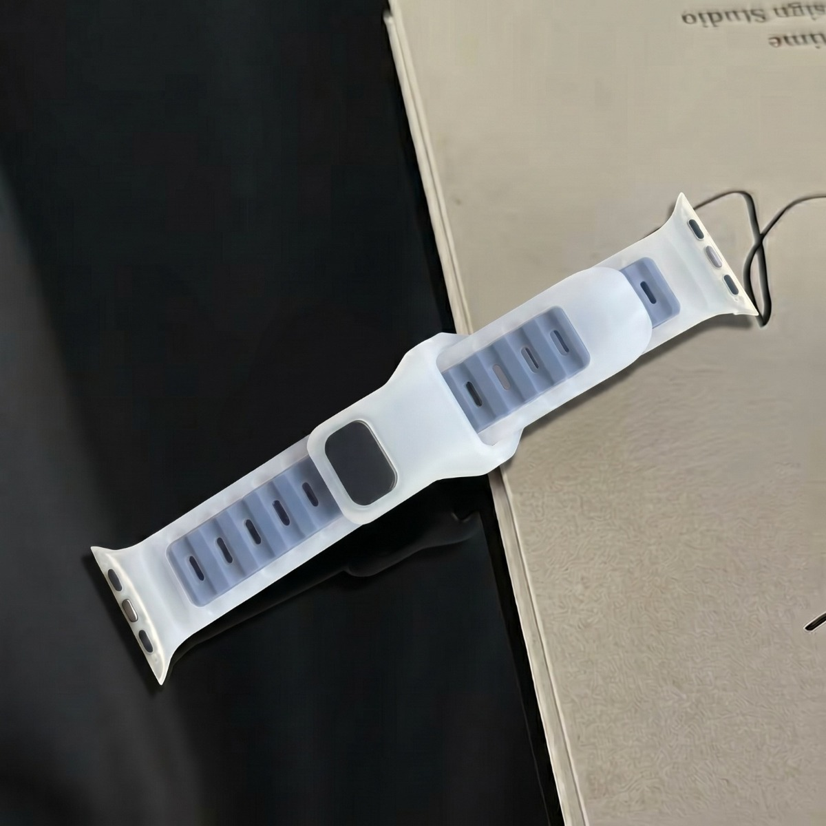 Ein weißes, gummiertes Smartwatch-Armband liegt auf einer dunklen Oberfläche neben einer beigefarbenen Broschüre.