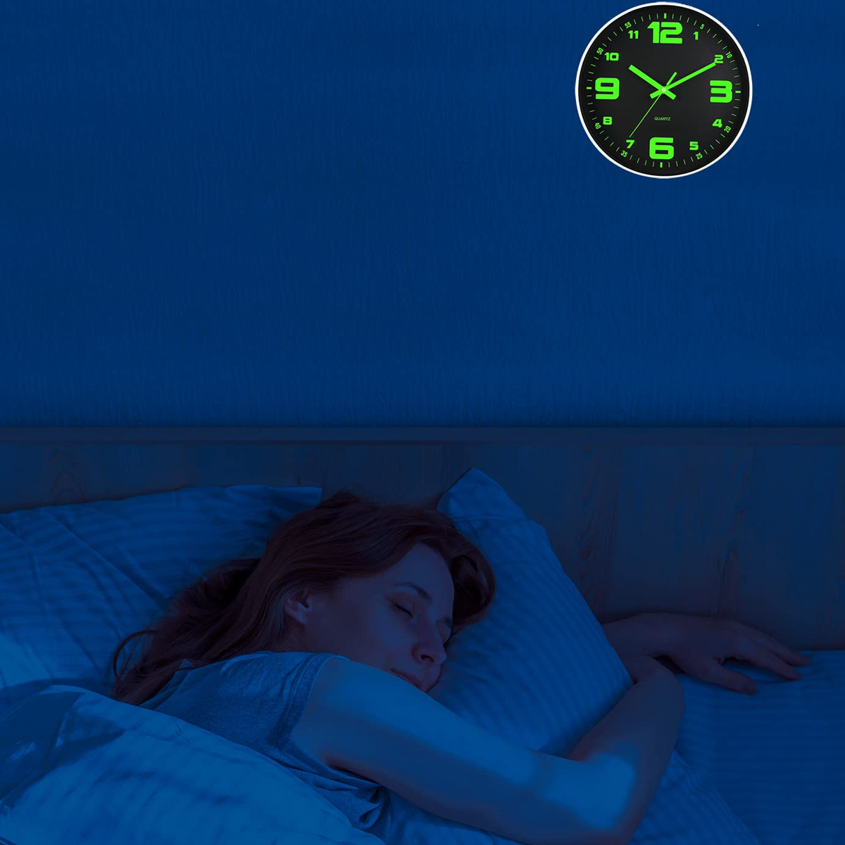 Eine Frau schläft im Bett, während an der dunklen Wand eine grün leuchtende Wanduhr hängt.