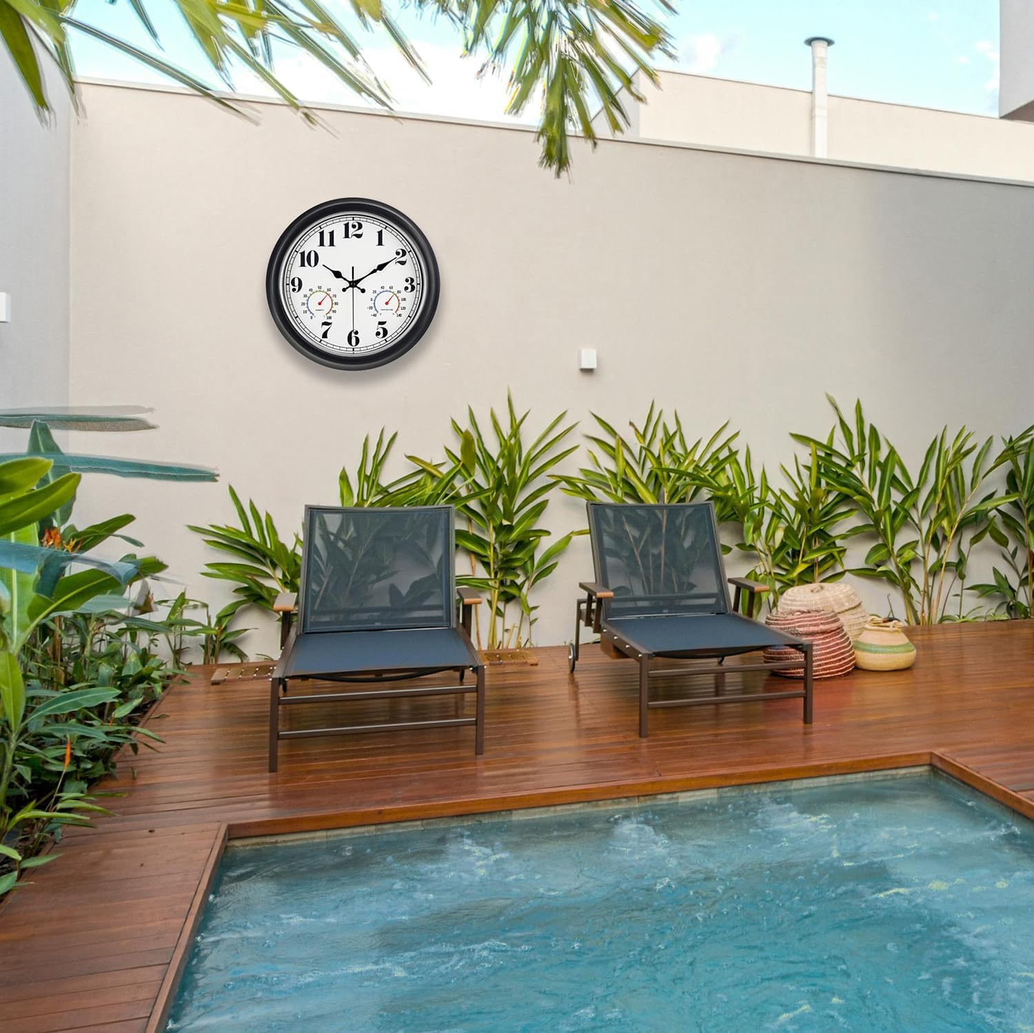 Eine Wanduhr hängt über zwei Liegestühlen an einer Poolterrasse mit Pflanzen.