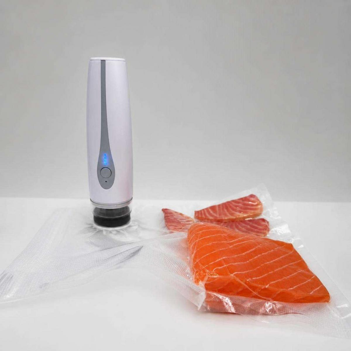 Ein weißes Vakuumiergerät versiegelt Plastiktüten mit rohen Lachsfilets auf einer weißen Oberfläche.