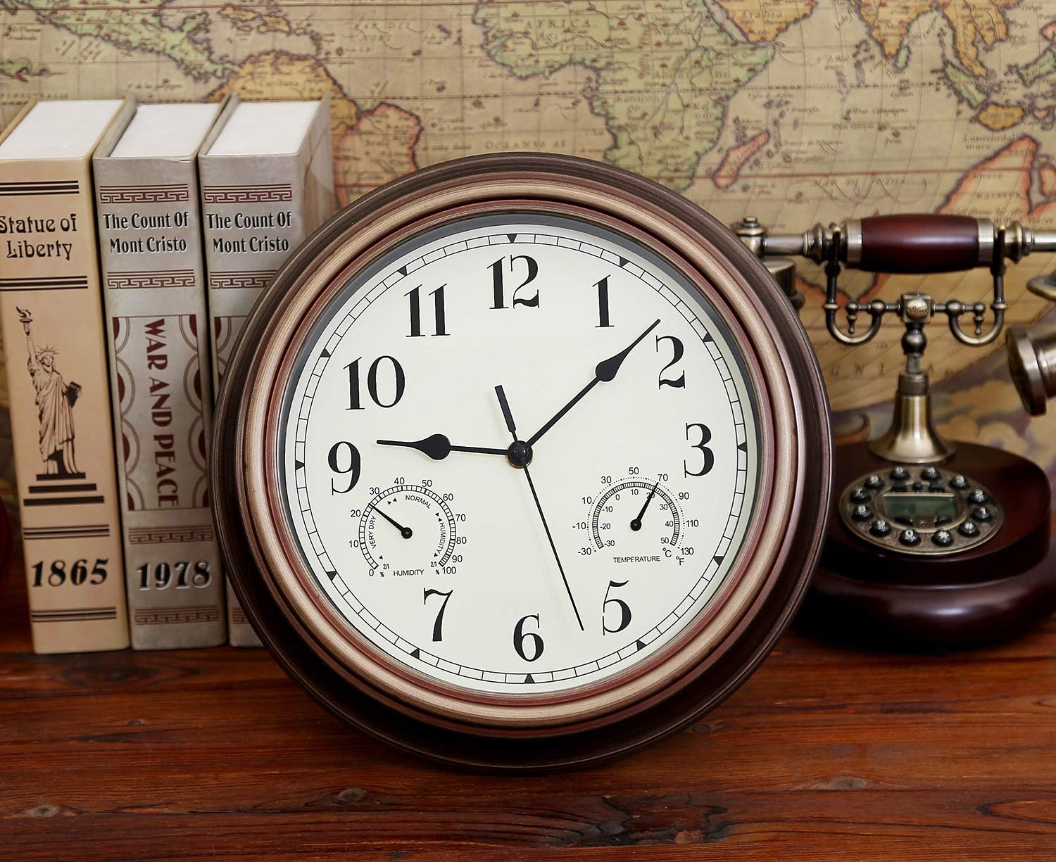 Eine runde Wanduhr mit Barometer steht auf einem Tisch vor Büchern und einer Weltkarte.