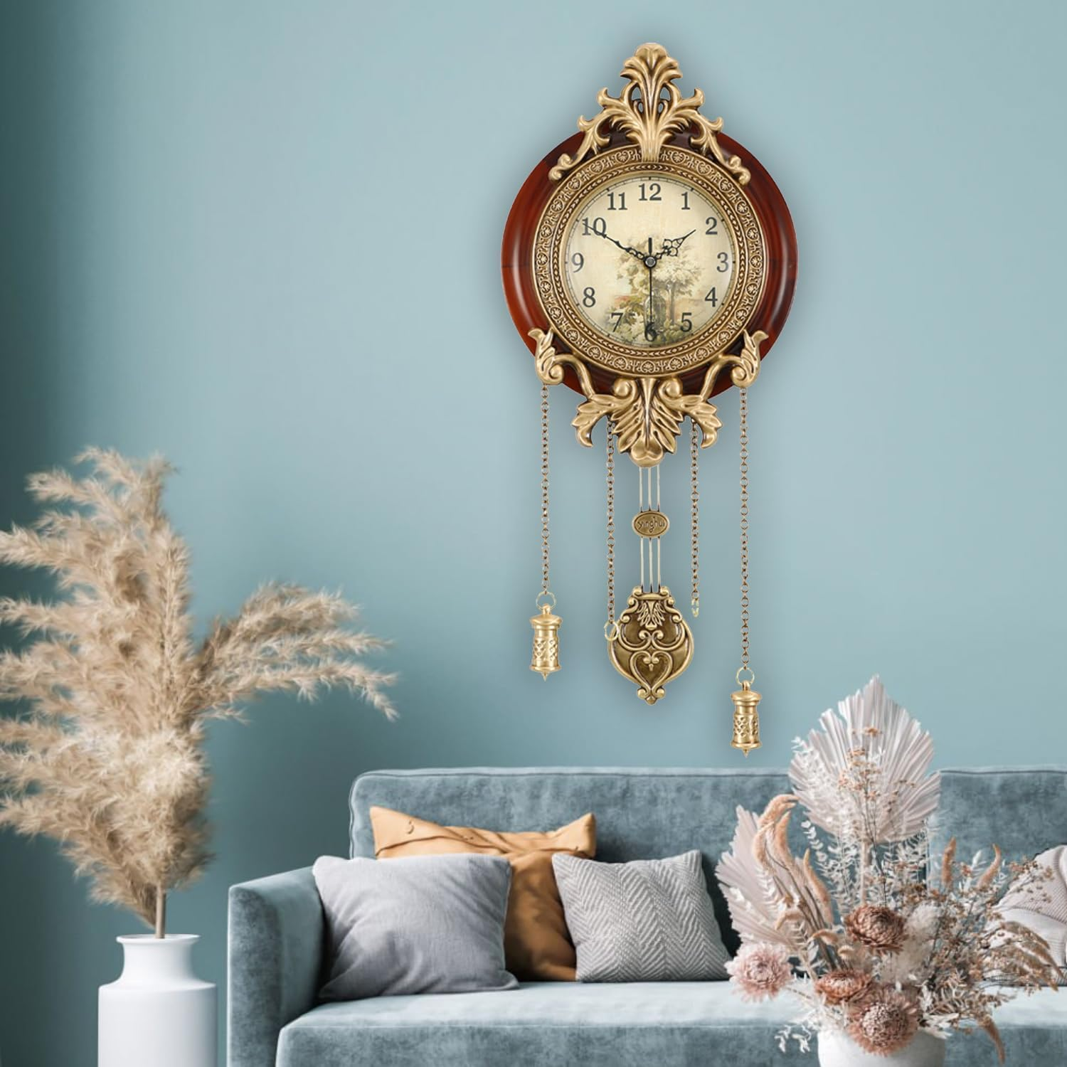 Eine ornate Wanduhr mit Holzrahmen und Hängedekor hängt über einem blauen Sofa mit Kissen und Trockenblumen.