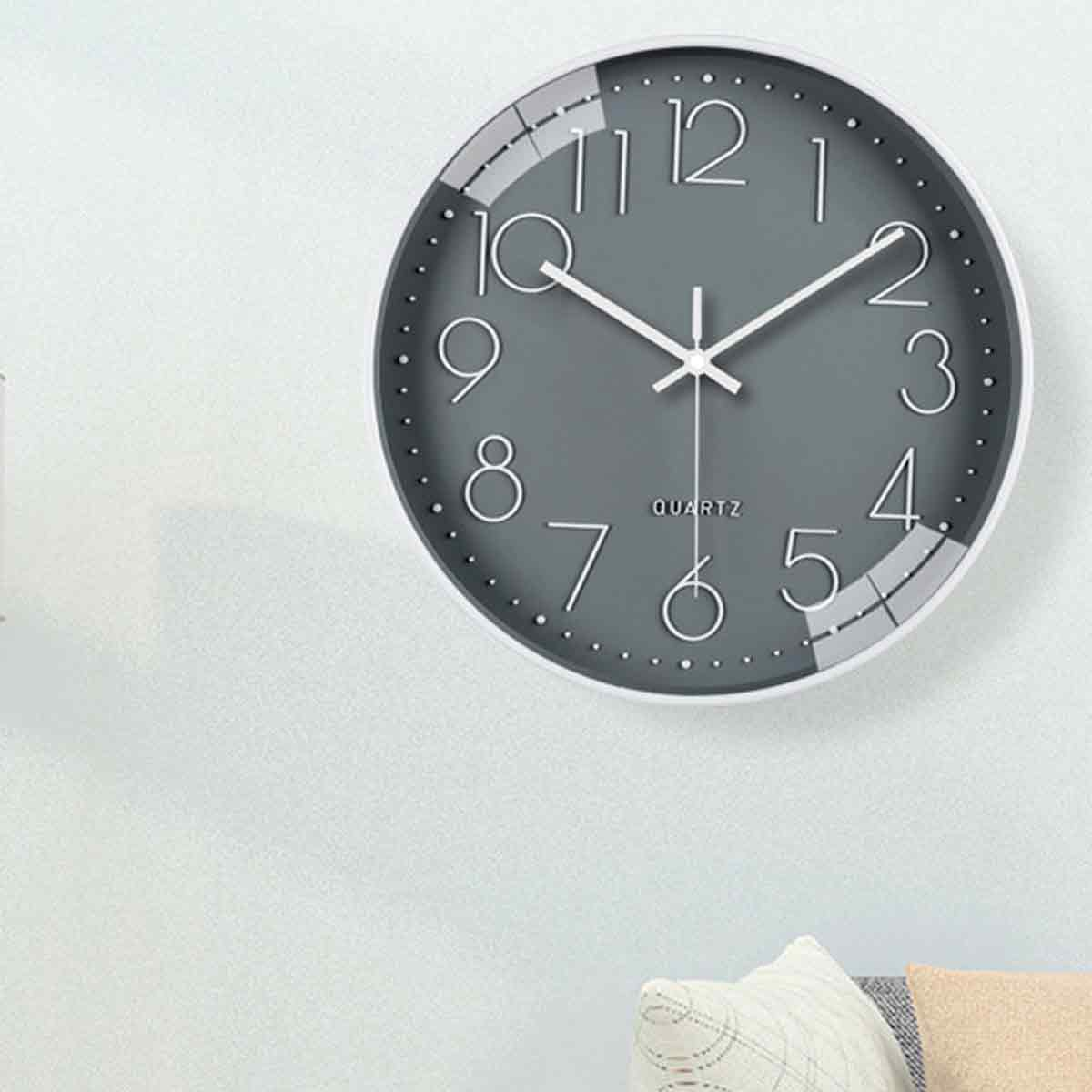 Eine runde Wanduhr mit grauem Zifferblatt und weißen Zahlen hängt an einer hellen Wand.