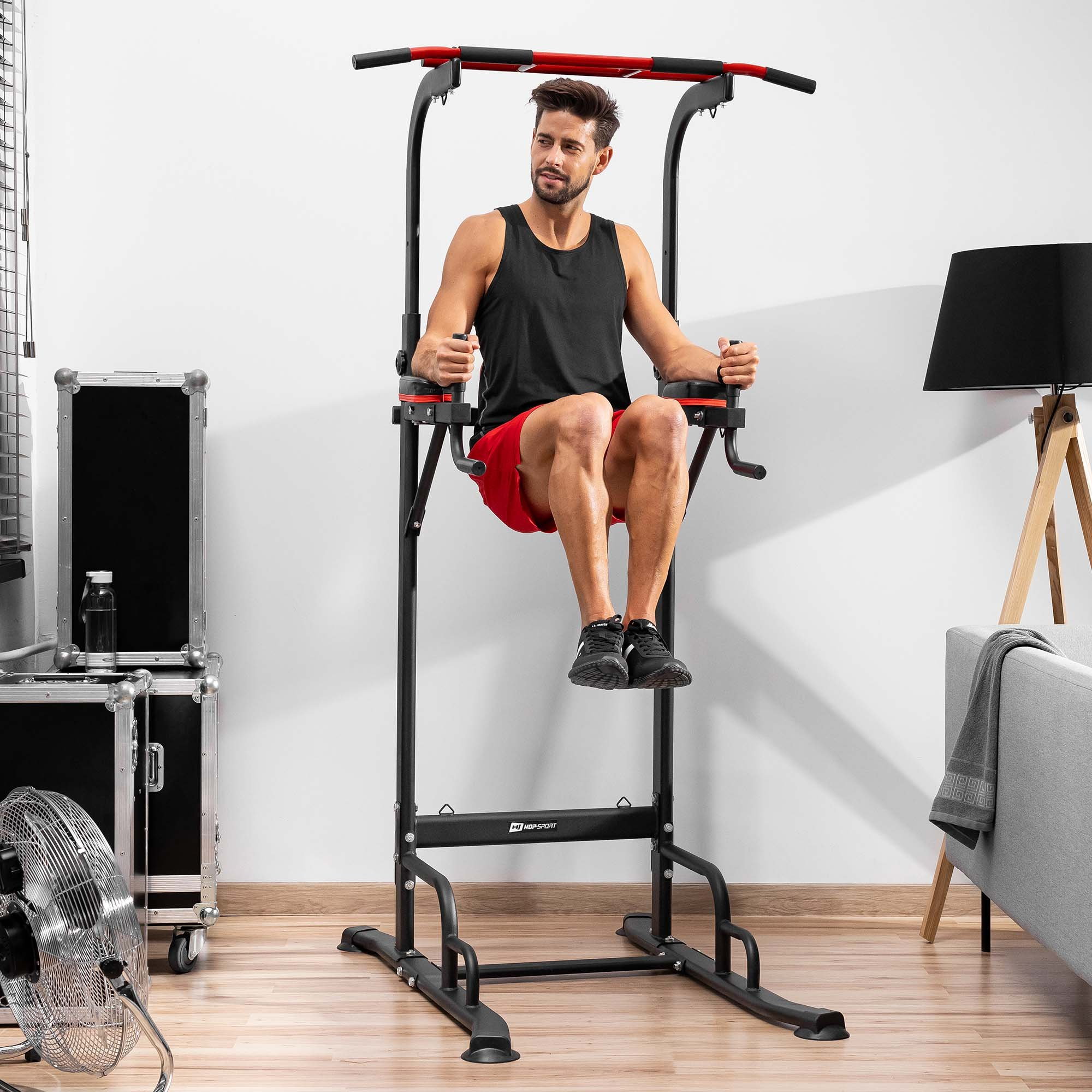 Ein Mann in Sportkleidung macht Knieheben an einer schwarzen Klimmzug- und Dip-Station in einem hellen Raum.