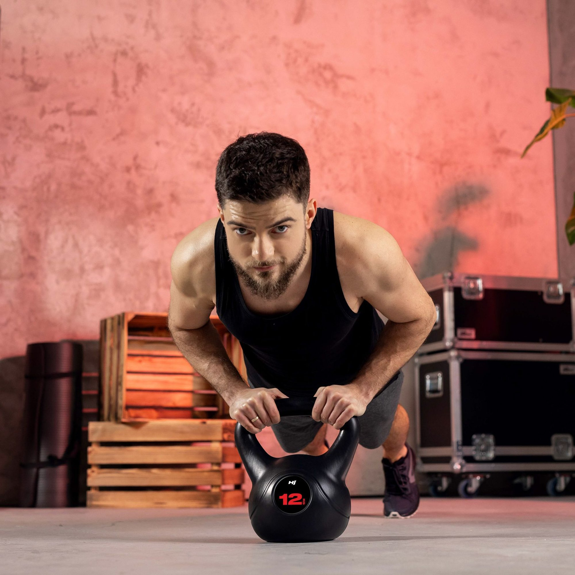 Ein Mann mit Bart macht Liegestütze auf einer Kettlebell in einem Fitnessstudio vor einer roten Wand.