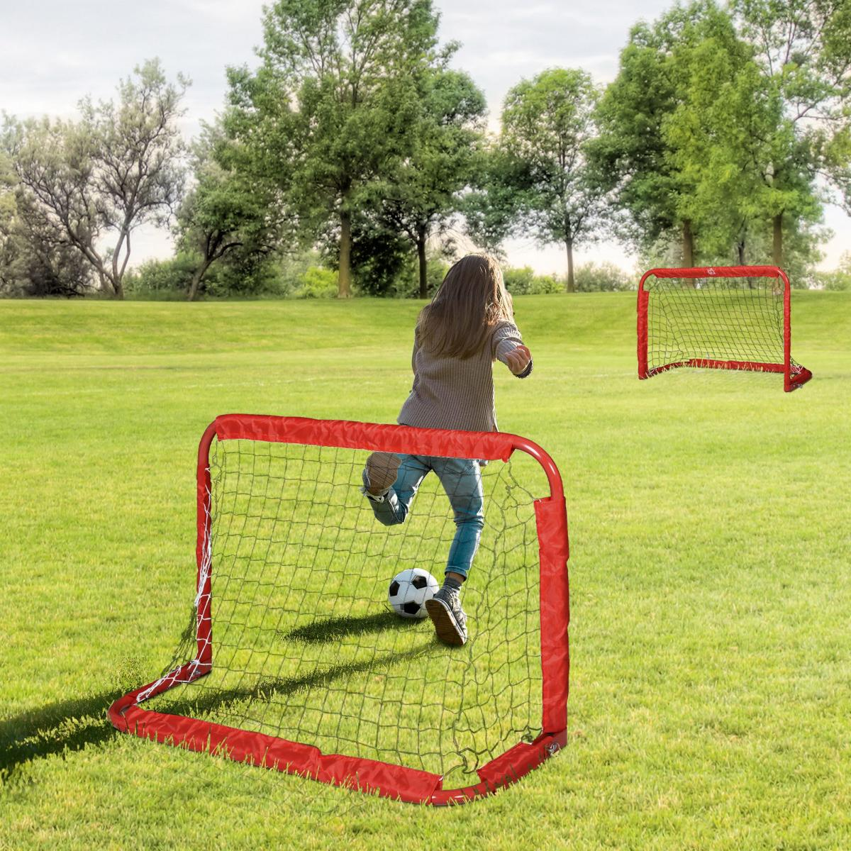 Ein Kind schießt auf einem grünen Feld einen Fußball in ein kleines rotes Tor.