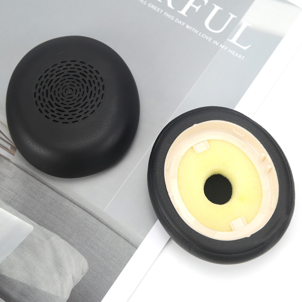 Two black headphone earpads on a surface, one showing the outer grille and the other the inner yellow foam.