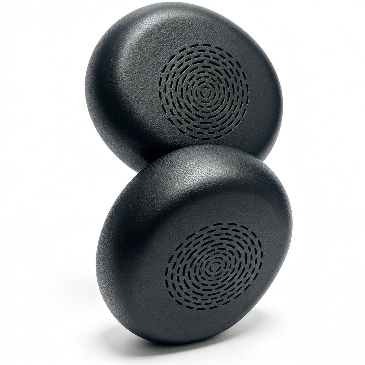 Two black leather earpads with circular speaker grilles stand on a white surface.