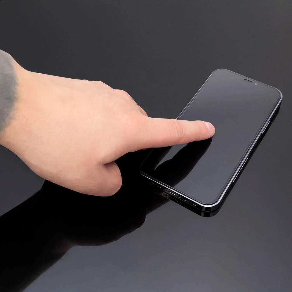 Una mano che tocca uno smartphone nero su una superficie scura e riflettente.