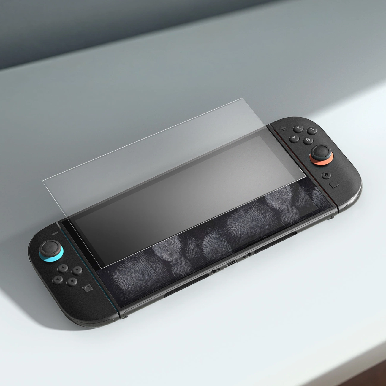 Una console portatile si trova su una superficie bianca mentre una pellicola protettiva in vetro viene applicata sullo schermo.