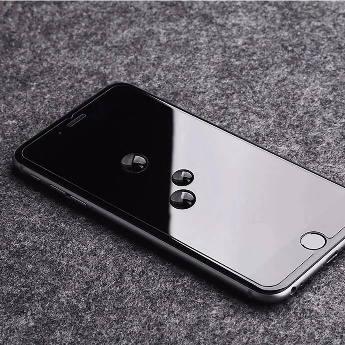Uno smartphone nero con gocce d'acqua sullo schermo poggia su una superficie di tessuto grigio.