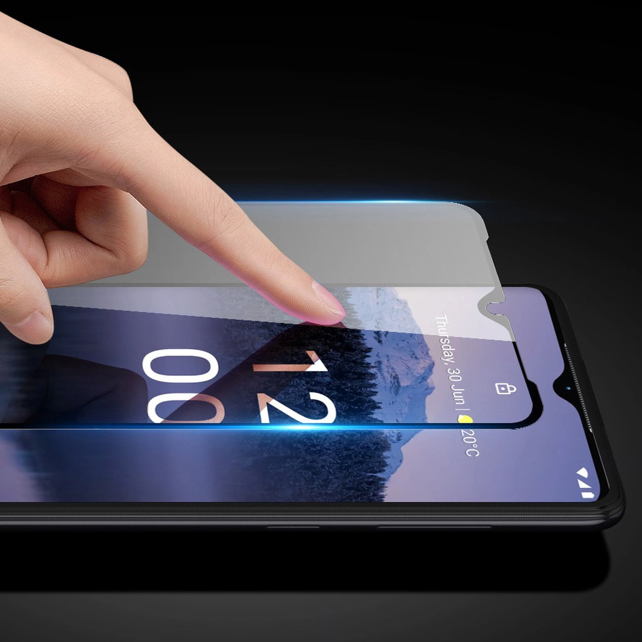 Una mano applica una pellicola protettiva su uno smartphone nero che mostra data e ora.