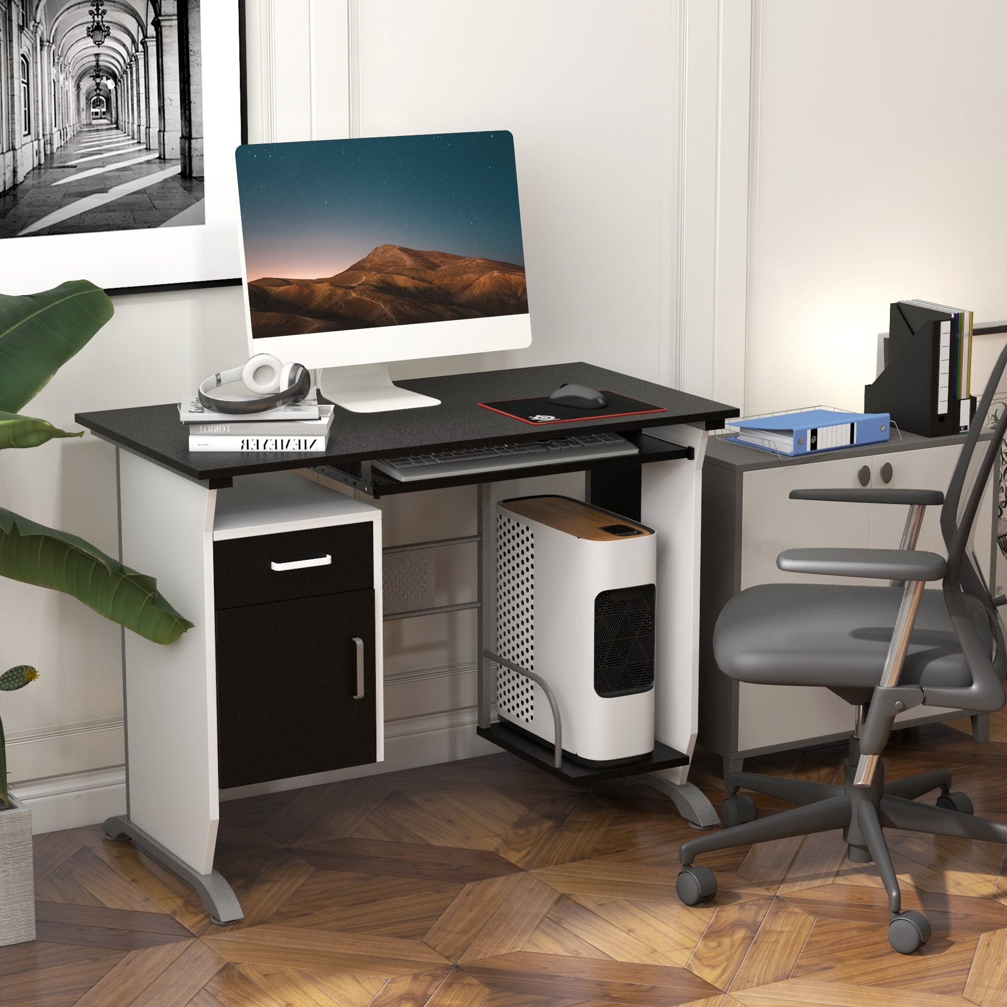 Una scrivania per computer nera e bianca con torre PC, monitor e sedia da ufficio su pavimento in legno.