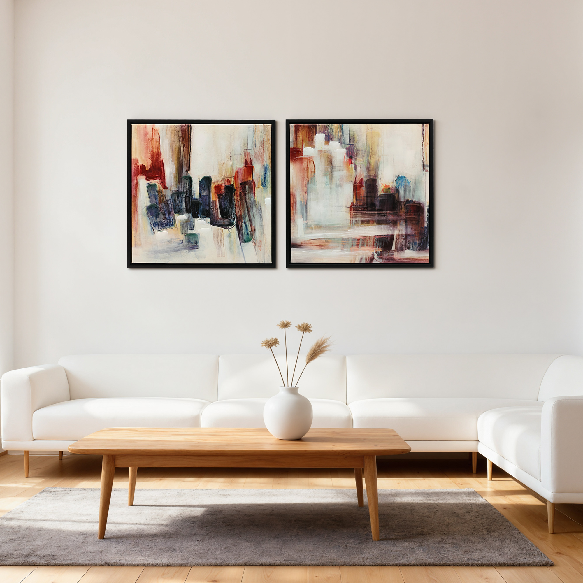 Un sofá blanco frente a una pared blanca con dos cuadros abstractos y una mesa de centro con un florero.