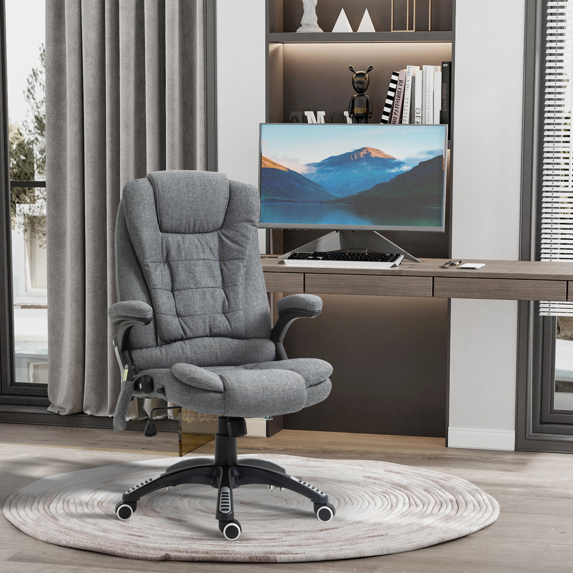 Una sedia da ufficcio grigia su un tappeto rotondo davanti a una scrivania in legno con monitor.