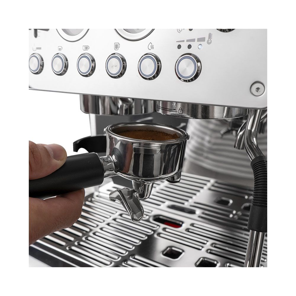 Une main tient un porte-filtre rempli de café moulu devant une machine à espresso en inox.