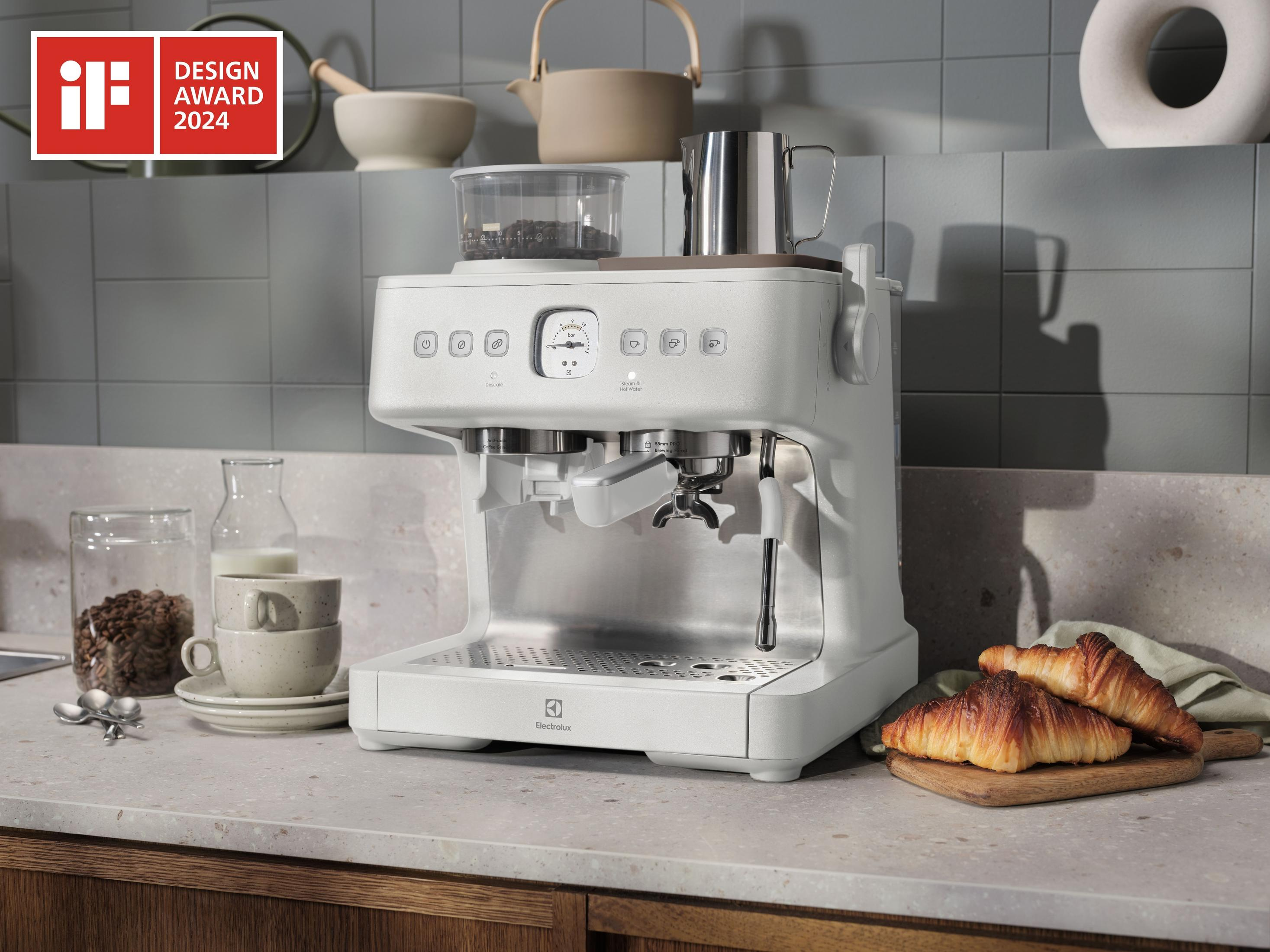 Una macchina da caffè bianca sul bancone con croissant, chicchi di caffè e tazze.