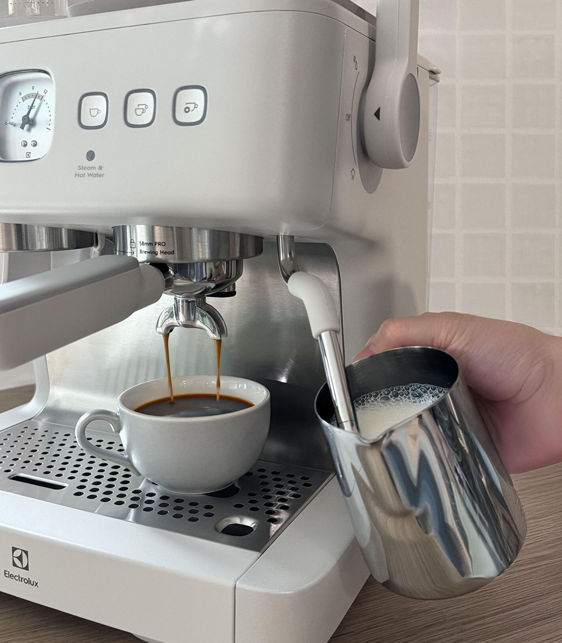 Una macchina da caffè bianca versa il caffè in una tazza mentre monta il latte in una lattiera.