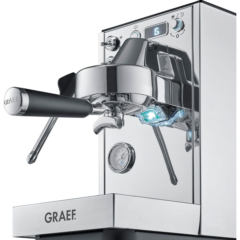 Une machine à espresso moderne en chrome avec porte-filtre noir, buses vapeur, manomètre et écran numérique.