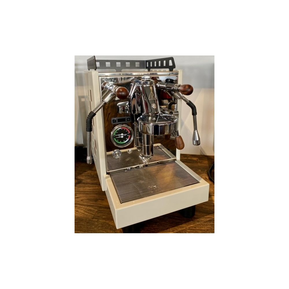 Una macchina da caffè espresso bianco crema e cromata con dettagli in legno su una superficie in legno.