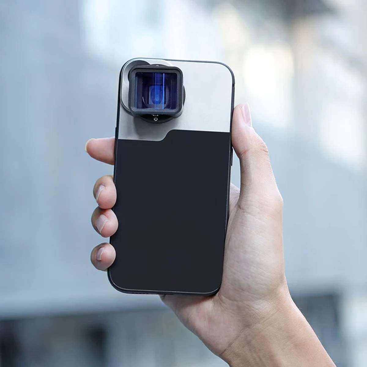 Eine Hand hält ein schwarzes und silbernes Smartphone mit einer quadratischen Kameraaufsatzlinse.