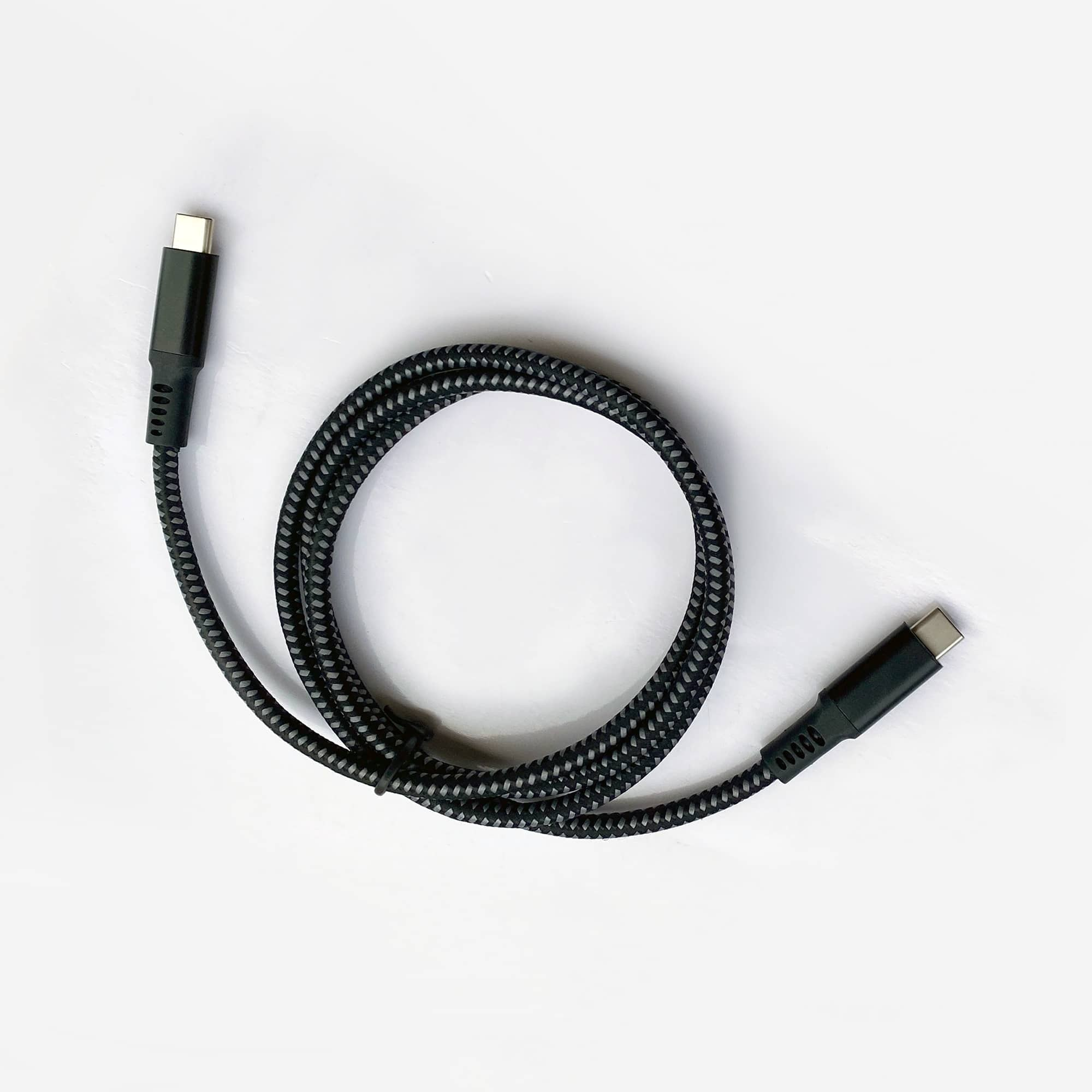 Un câble USB-C tressé noir et gris repose sur une surface blanche.